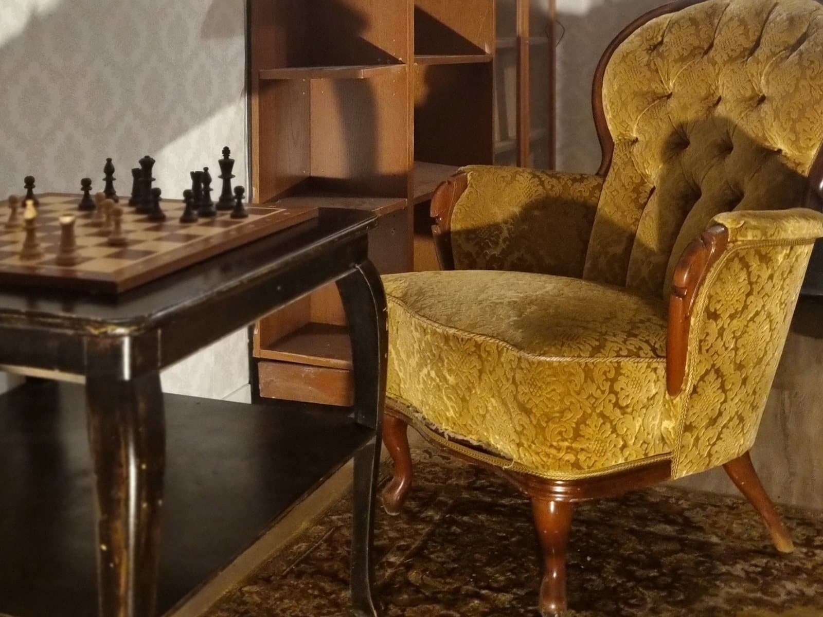 One of the Escape House rooms: a chessboard on a dark table next to a gold patterned armchair.